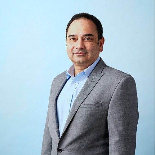 Portrait of Sriram in a gray blazer on a teal background, overlaid on a dynamic image of a road at night with light trails symbolizing speed and motion, alongside 5Flow branding.